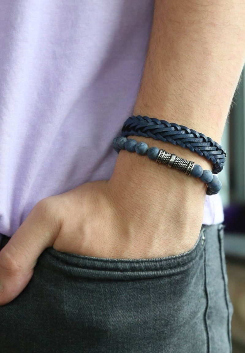 Marine leren gevlochten armband met zilveren accenten, gecombineerd met een kralenarmband met donkerblauwe stenen en zilveren details.