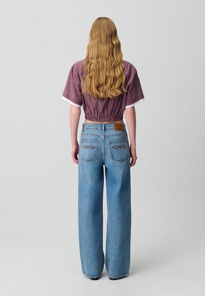 Top corto de algodón burdeos con cuadros y cintura fruncida, combinado con vaqueros de pierna ancha azul claro que presentan bordado en el bolsillo trasero y una etiqueta de cuero.