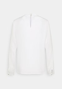 Weißes Langarmblusenshirt mit einem Schlüsselloch-Ausschnitt auf der Rückseite, rundem Halsausschnitt und Knopfakzenten an den Manschetten. Angenehm glattes und leichtes Material.