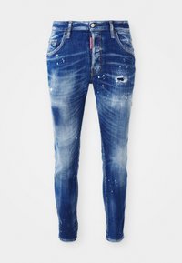 Jeans de mezclilla azul de corte ajustado con un lavado desgastado, detalles de manchas de pintura, parches desgastados y diseño de cinco bolsillos. Etiqueta de marca roja en la cintura.