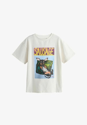 Weißes T-Shirt mit farbenfroher Grafik eines entspannten Hundes, der auf einem grünen Sofa liegt, und dem Wort „SAUSAGE“ in großen gelben Buchstaben darüber.