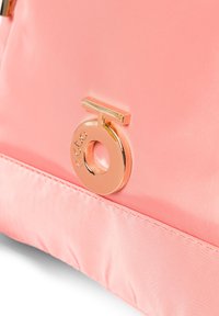 Borsa in satin rosa con accento del logo circolare dorato lucido e base rettangolare. Texture liscia e linee di design pulite.