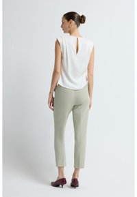 Hvid ærmeløs top med nøglehul i ryggen, parret med tætsiddende, lysegrønne bukser og maroon højhælede sko, set fra ryggen.