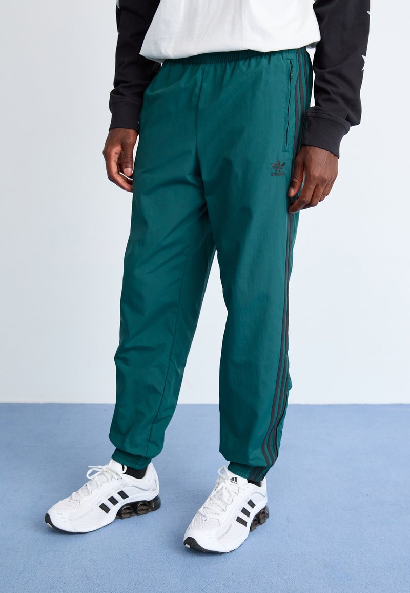 Teal lette bukser med elastisk midje, sidelommer med glidelås og svarte stripete detaljer. Kombinert med hvite treningssko.