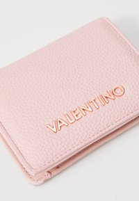 Ružová textúrovaná kožená peňaženka s embosovaným logom "VALENTINO" v ružovom zlate. Kompaktný obdĺžnikový tvar s zaoblenými hranami a prešívaním.
