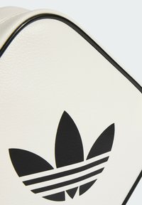 Bolsa sintética blanca con una superficie texturizada, que presenta un gran logo trefoil negro de Adidas y ribetes negros a lo largo de los bordes.