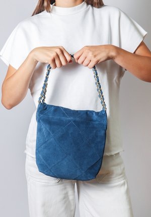 Borsa in pelle scamosciata blu con un design trapuntato, dotata di una tracolla a catena intrecciata in oro. La borsa ha una consistenza morbida e una forma arrotondata.