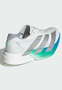Biele bežecké topánky so striebornými akcentmi, gradientovou teal podrážkou a štruktúrovaným zvrškom. Obsahujú bezpečný systém šnúrovania a branding na boku.
