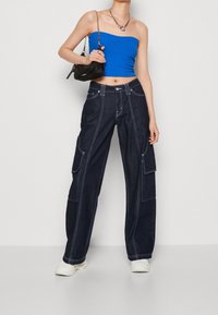 Blå ribbad kort topp med raka mörka denim cargo byxor som har vit sömnad och sidofickor. Svart axelremsväska med kedjesnodd.