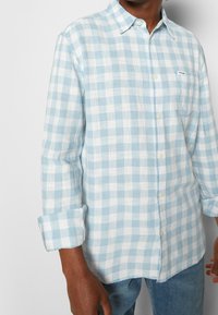 Ljusblå och vit rutigt skjorta med button-down-krage, uppvikta ärmar, bomullsmaterial och en liten ficka på vänster bröst.