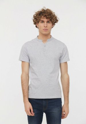 Chemise à manches courtes de style Henley en coton gris clair, avec un col rond et trois boutons, associée à un jean bleu foncé.