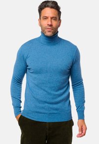 Blauer Rollkragenpullover aus strukturiertem Strickstoff, mit langen Ärmeln und enger Passform, kombiniert mit dunkelgrünen Cordhosen.