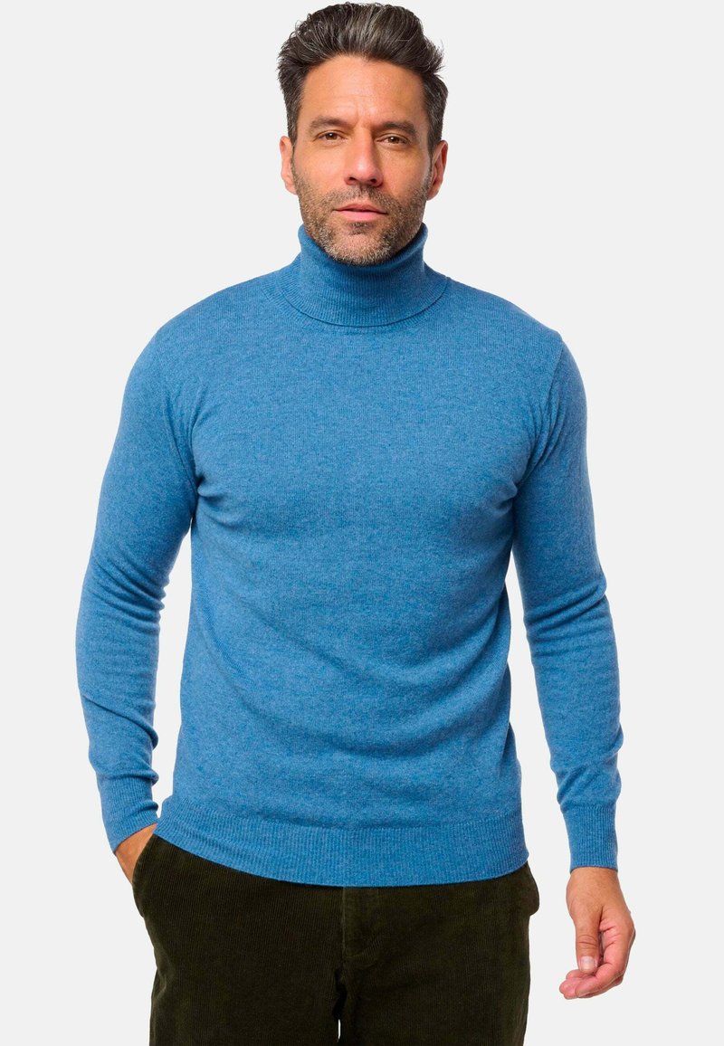 Blauer Rollkragenpullover aus strukturiertem Strickstoff, mit langen Ärmeln und enger Passform, kombiniert mit dunkelgrünen Cordhosen.