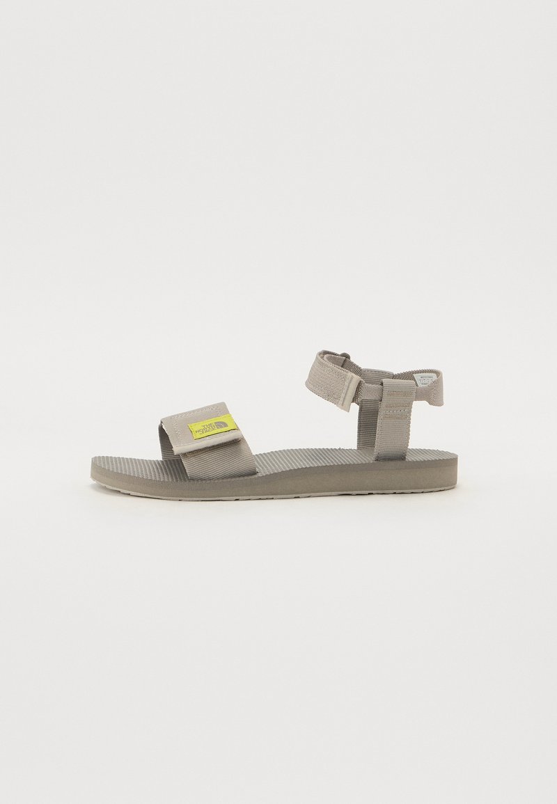 Grey sandal with adjustable strap, textured sole, and small yellow logo detail. Made from synthetic material with a flat design.