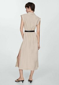 Abito midi beige con maniche corte, cintura, e spacchi laterali. Tessuto liscio con una leggera texture; design minimalista. Dettaglio della cintura nera.