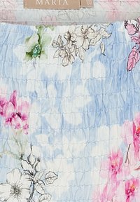 Blomstermønsteret stof med lyseblå baggrund, lyserøde og hvide blomster samt en tekstureret, smocket design for ekstra detaljer.