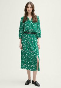 Vestido verde con un estampado floral, con escote en V, mangas 3/4, abertura lateral y un cinturón negro. Combinado con mocasines negros.