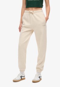 Pantalons de survêtement en coton beige avec une taille élastique et des poignets, dotés de poches latérales et d'un petit logo brodé sur la jambe.