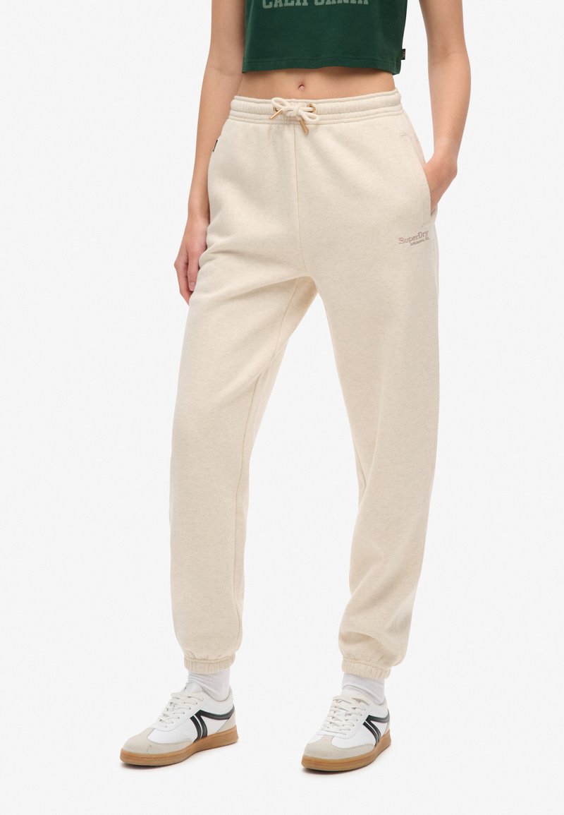 Pantalons de survêtement en coton beige avec une taille élastique et des poignets, dotés de poches latérales et d'un petit logo brodé sur la jambe.