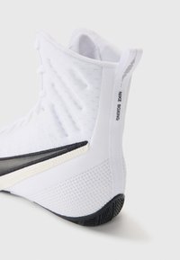 White high-top boxing shoe with textured mesh upper, black accent along the midsole, and distinctive branding on the heel tab.