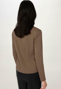 Haut marron à manches longues avec un col rond et une texture lisse, associé à un pantalon noir. Présente un design simple et ajusté. Aucune motif visible.