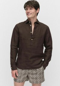 Chemise en lin marron à manches longues avec patte de boutonnage partielle, associée à un short beige à motifs avec des designs géométriques.