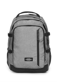 Mochila gris con acentos negros, múltiples compartimentos con cremallera, textura de tela, bolsillos de malla en los laterales y una asa superior para llevar.
