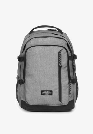 Sac à dos gris avec des accents noirs, plusieurs compartiments zippés, texture en tissu, poches latérales en mesh et une poignée supérieure pour le transport.