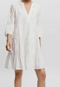 Vit bomulls klänning med avslappnad passform, V-ringning, trekvartsärmar och flerårig volangnederdel; har broderade ögonblicksmönster.