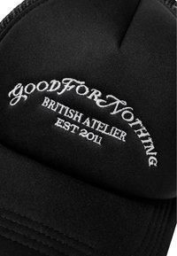 Cappello nero in tessuto con testo ricamato bianco: "goodForNothing," "BRITISH ATELIER," e "EST 2011." Parte superiore arrotondata con dettaglio di cuciture.