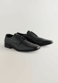 Fekete bőrből készült dresszcipők hegyes orral, fűzős kialakítással, lapos talppal és minimalista stílussal, sima tapintással és finom varrással.