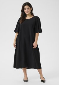 Abito nero fino al ginocchio con scollatura tonda e maniche a sbuffo corte. Realizzato in un tessuto morbido, presenta una vestibilità ampia e rilassata.