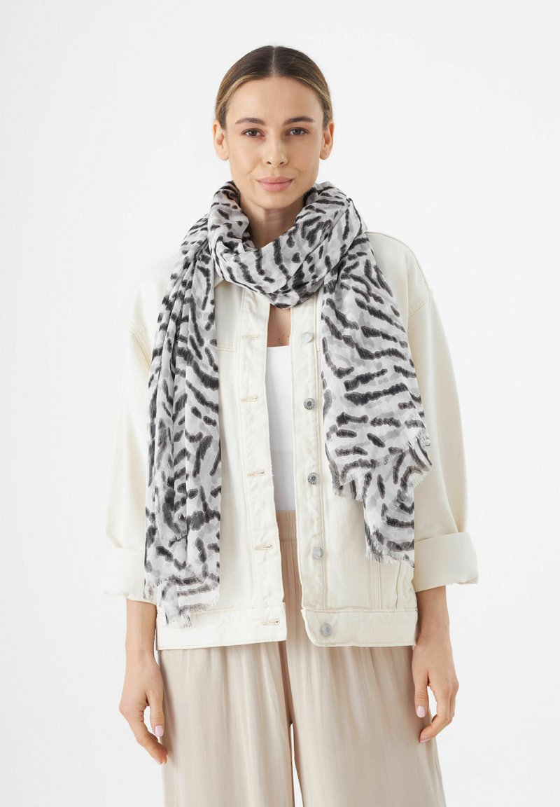 Foulard à motifs animaliers noir et gris en tissu léger, avec des bords effilochés. Porté lâchement autour du cou par-dessus un haut blanc.