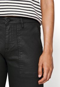 Pantalones de mezclilla negros con un bolsillo frontal, presillas para el cinturón y un cierre de botón. Textura suave con costuras y detalles de puntadas sutiles.
