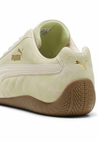 Zapatilla deportiva Puma en ante de color verde claro con un acabado texturizado, detalles en blanco y suela de goma con un patrón de banda de rodadura en zigzag. Acentos del logo en dorado.