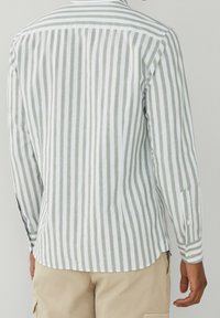 Langærmet skjorte med grønne og hvide lodrette striber. Fremstillet af lette materialer med buet kant, manchetknapper og krave.