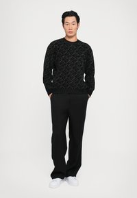 Pulover negru texturat cu un model complicat, asortat cu pantaloni negri cu dungi subțiri și adidași albi.