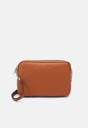 Rechthoekige bruine leren polstasje met gouden kettingdetail en Calvin Klein-logo aan de voorkant tegen een witte achtergrond.