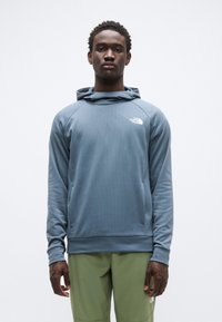 Φωτεινή γαλάζια φούτερ με κουκούλα από υφασμάτινη υφή, με μπροστινή τσέπη και κουκούλα. Διαθέτει λευκό λογότυπο στο πάνω αριστερό μέρος. Συνδυάζεται με πράσινο παντελόνι.