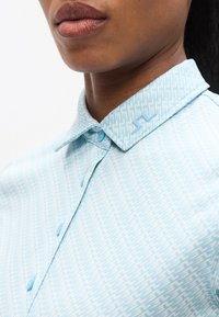 Φωτεινό γαλάζιο πουκάμισο με κουμπιά, με υφασμένο μοτίβο γεωμετρικών σχημάτων, με μυτερό γιακά και γαλάζια κουμπιά.