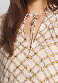 Light fabric top featuring a neutral base with a yellow and navy geometric pattern, deep V-neck, and a tie closure at the collar.