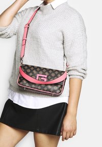 Sac bandoulière avec un extérieur noir à motif, des accents en cuir rose et une sangle ajustable. Dispose d'un fermoir en forme de G en métal.