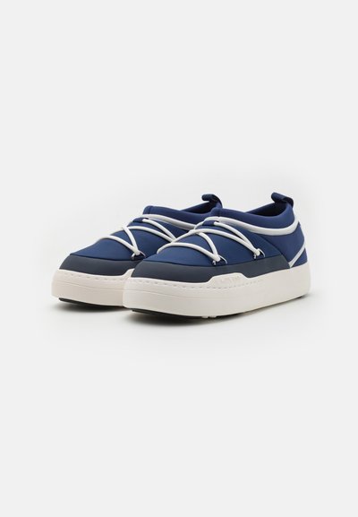 Sneakers bleumarin cu un exterior din țesătură texturată, șireturi albe și o talpă groasă de culoare crem. Au un design elegant, cu un profil jos.