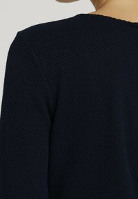 Granatowy sweter z fakturowanym wzorem w zygzaki, z okrągłym dekoltem i długimi rękawami, podkreślający solidny materiał dzianinowy.