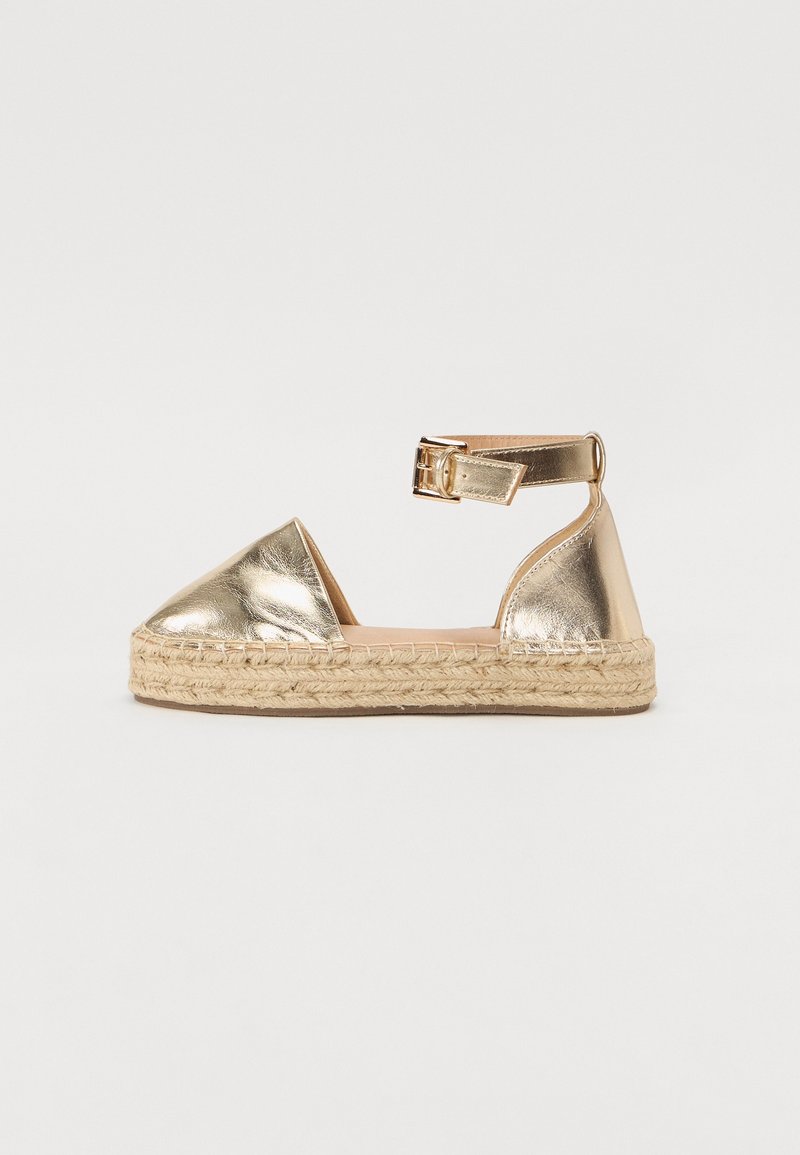 Espadrille plate métallique dorée avec bout fermé, bride de cheville, fermeture à boucle et semelle plateforme en jute tissé.