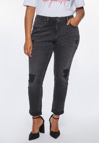 Black denim jeans with distressed detailing, rhinestone accents, and rolled cuffs. Worn with black high-heeled sandals.