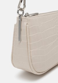 Sac à main beige avec un motif croco, d'une texture lisse, doté d'une fermeture éclair et de quincaillerie en argent, et d'une forme structurée.