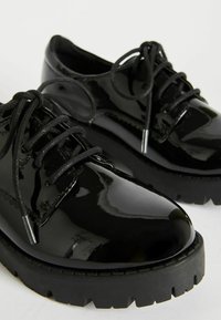 Scarpe in pelle verniciata nera con punta tonda, suola in gomma spessa, design con lacci e lacci neri a contrasto. Superficie lucida con dettagli di cucitura visibili.