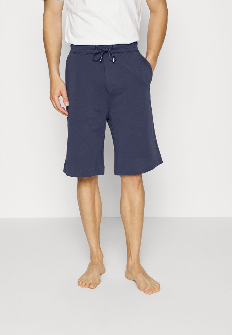 Os calções de algodão azul marinho apresentam uma cintura com cordão ajustável, bolsos laterais e um corte relaxado, que se estende logo acima dos joelhos.