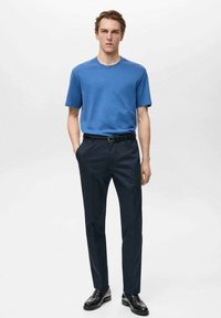 Tricou albastru din bumbac cu guler rotund, mâneci scurte, asortat cu pantaloni negri, adaptați, și pantofi din piele negri. Textură netedă, design mulat.